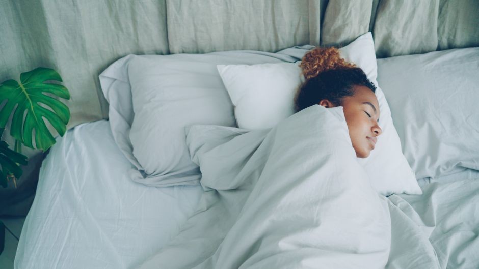 Seorang wanita tidur nyenyak di kamar tidur minimalis yang nyaman dengan seprai putih.