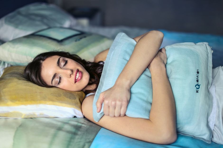 Seorang wanita tidur nyenyak di tempat tidur memeluk bantal lembut, membangkitkan rasa nyaman dan relaksasi.
