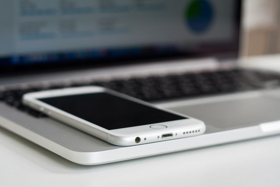 Perangkat laptop dan smartphone mengisi daya di meja kerja