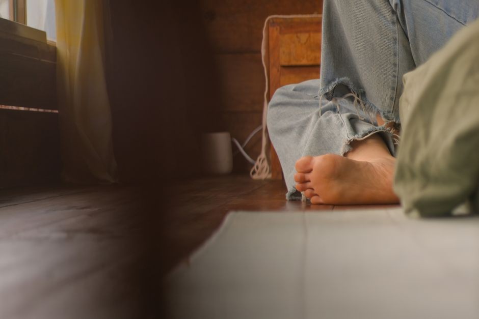 Setting dalam ruangan yang nyaman dengan orang santai berpakaian denim, bertelanjang kaki, menikmati suasana pagi yang tenang.
