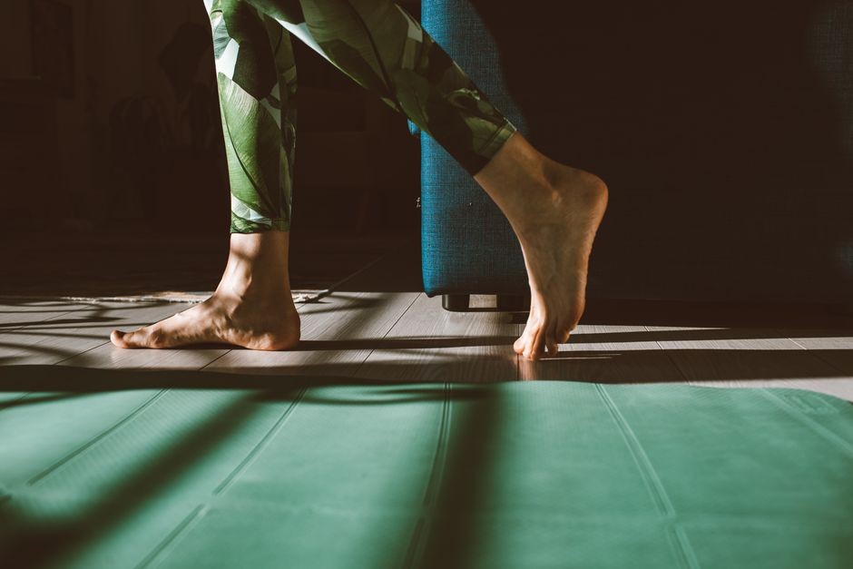 Kaki telanjang melangkah ke mat yoga di ruangan yang terang oleh sinar matahari dengan legging hijau cerah yang membentuk bayangan.