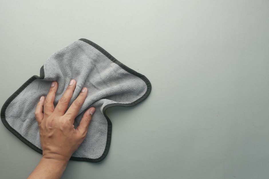 Sebuah tangan mengelap meja berwarna terang dengan kain mikrofiber abu-abu, ideal untuk konsep pembersihan.