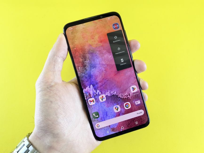 Gambar close-up tangan yang memegang telepon pintar dengan wallpaper abstrak berwarna-warni pada latar belakang kuning.
