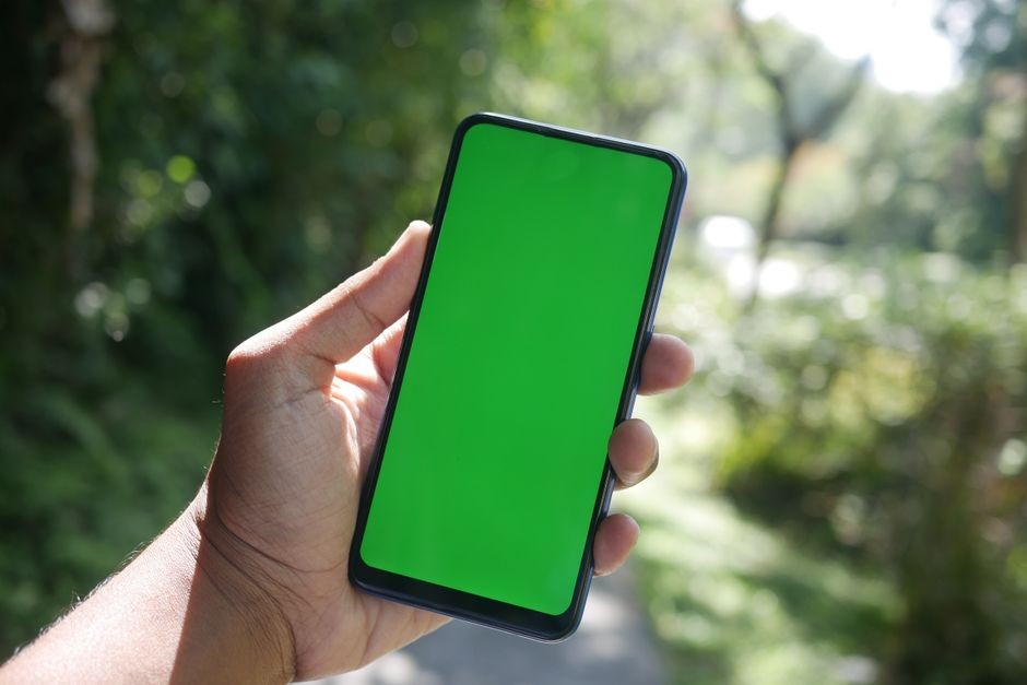 Seseorang memegang ponsel pintar di bawah terik sinar matahari luar ruangan dengan layar jelas