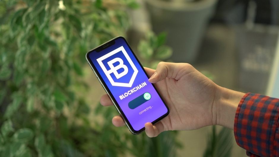 Close-up smartphone yang menunjukkan layar aplikasi blockchain yang dipegang oleh sebuah tangan.