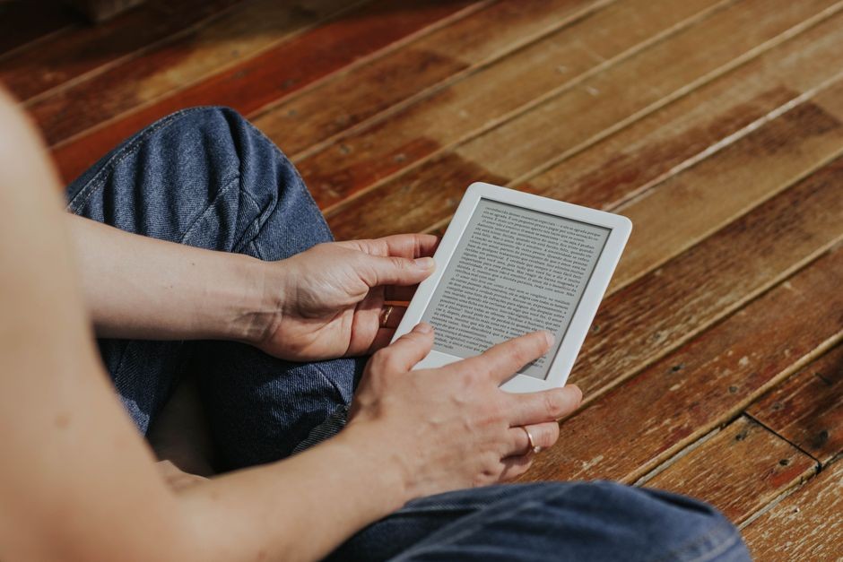Seseorang sedang membaca buku digital pada perangkat e-reader dengan layar e-ink yang teduh di mata