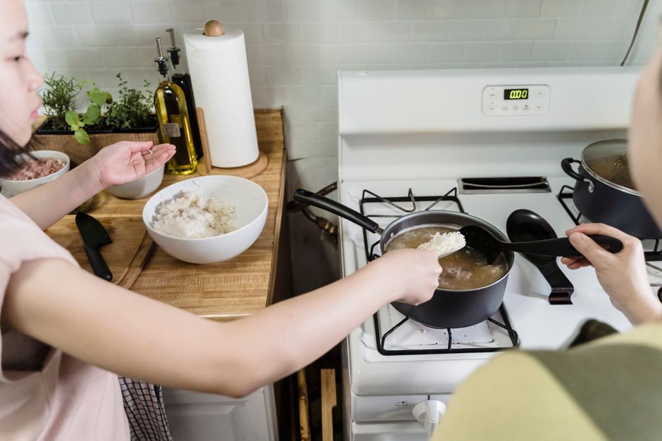 Seorang ibu dan anak perempuannya memasak nasi bersama di atas kompor, mempererat ikatan keluarga di dapur.