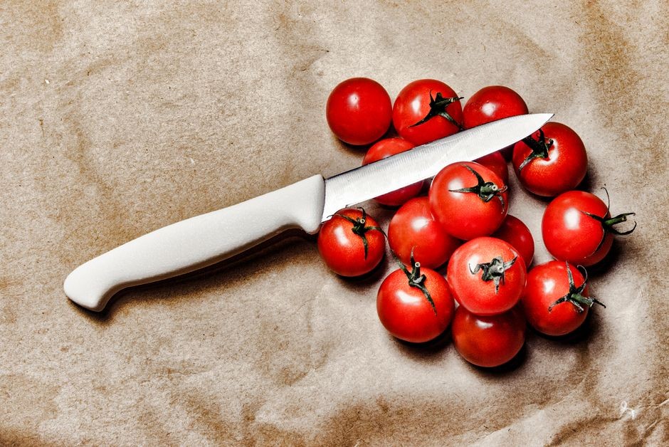 Seseorang mengiris tomat segar di atas talenan dapur dengan pisau