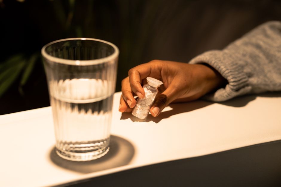 Seseorang memegang segelas air dan obat pil pereda nyeri sebelum diminum