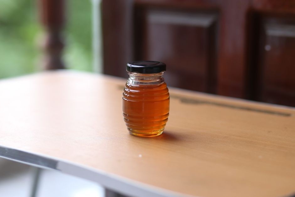 Toples kaca berisi madu murni berwarna keemasan di atas meja kayu dapur yang hangat