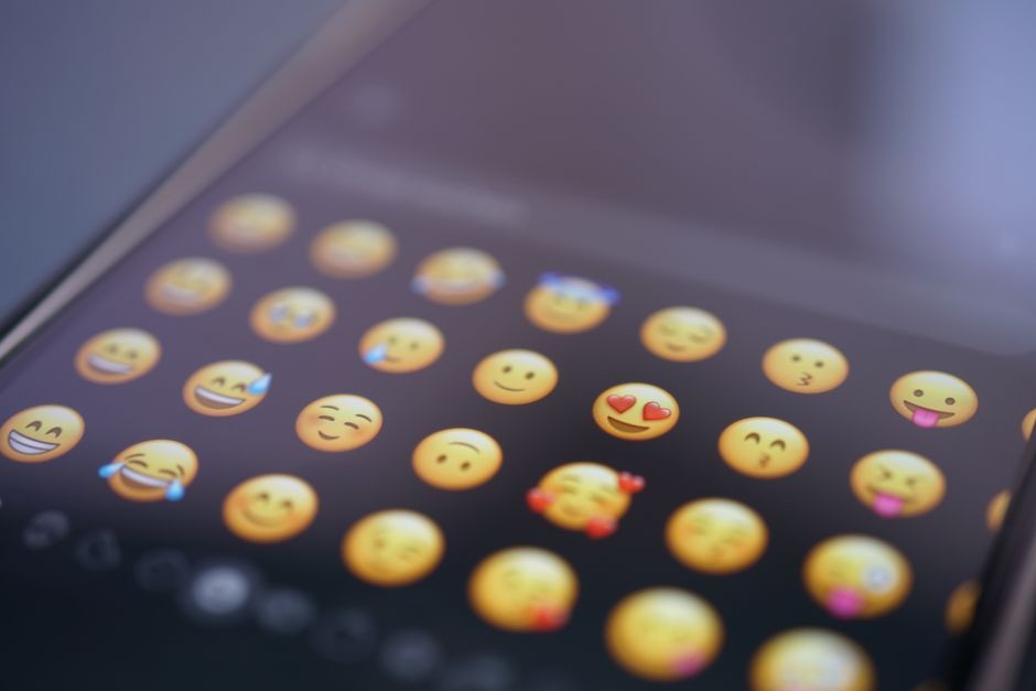 Tampilan dekat berbagai emoji di layar telepon pintar, melambangkan komunikasi digital dan penggunaan media sosial.