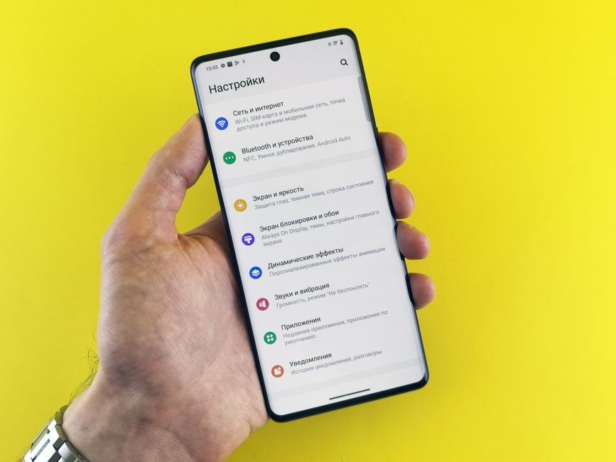 Tampilan dekat tangan yang memegang telepon pintar dengan menu pengaturan pada latar belakang kuning cerah.