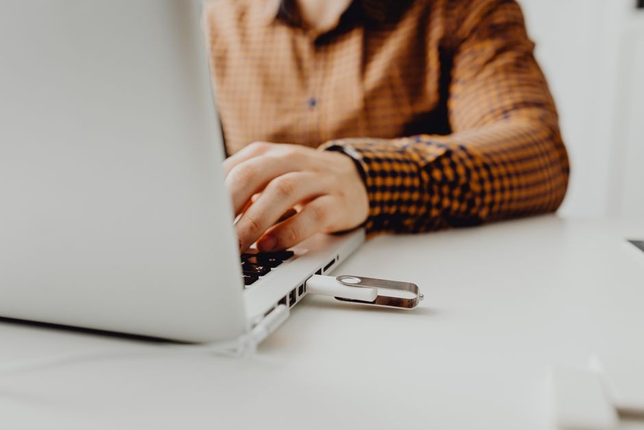 Seseorang yang bekerja di laptop dengan flash drive USB terhubung, mewakili teknologi dan penyimpanan data.