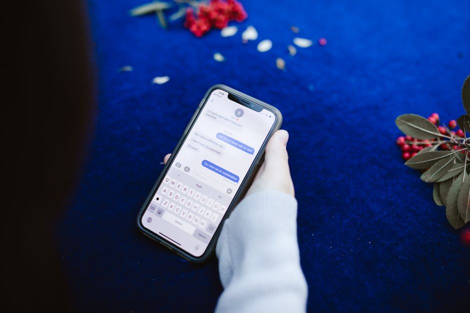 Seseorang memegang smartphone yang menampilkan pesan teks di permukaan biru dengan bunga.