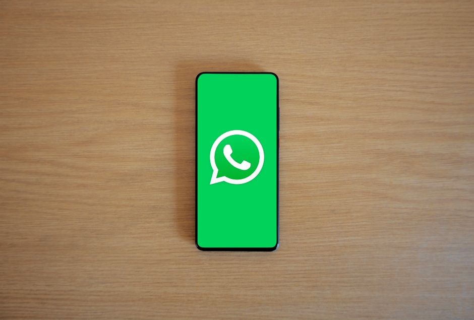 Tampilan atas smartphone menampilkan logo WhatsApp di latar belakang kayu, mewakili teknologi dan komunikasi.