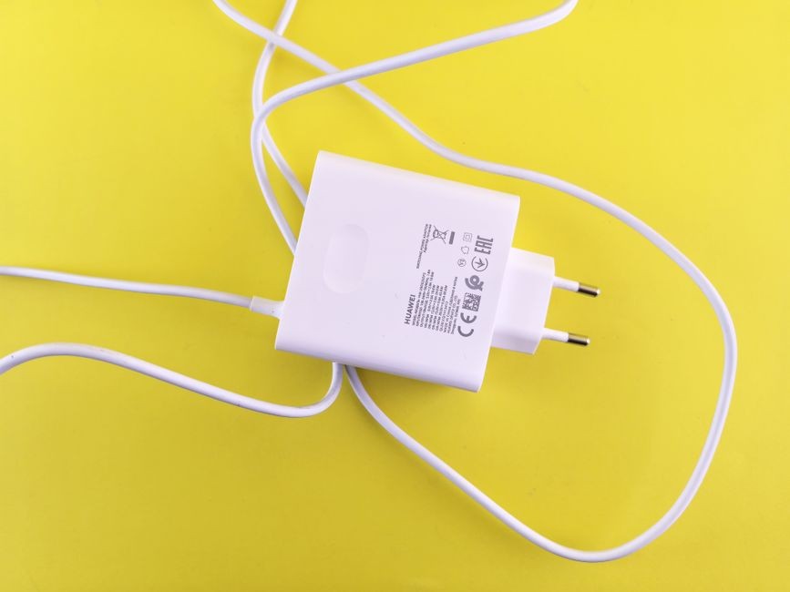 Pengisi daya USB putih dengan kabel di permukaan kuning cerah, menonjolkan desain aksesori teknologi.