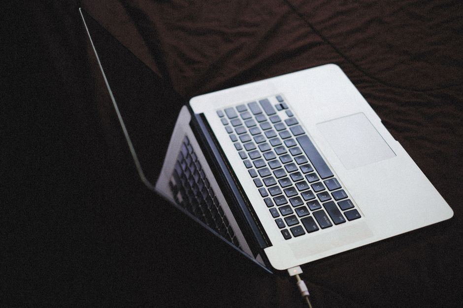 Laptop modern dengan keyboard backlit di permukaan kain gelap, terhubung ke pengisi daya.