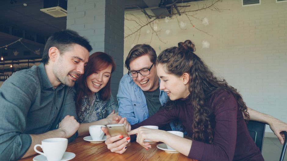 Empat sahabat tertawa dan berbagi momen sambil minum kopi di sebuah kafe.